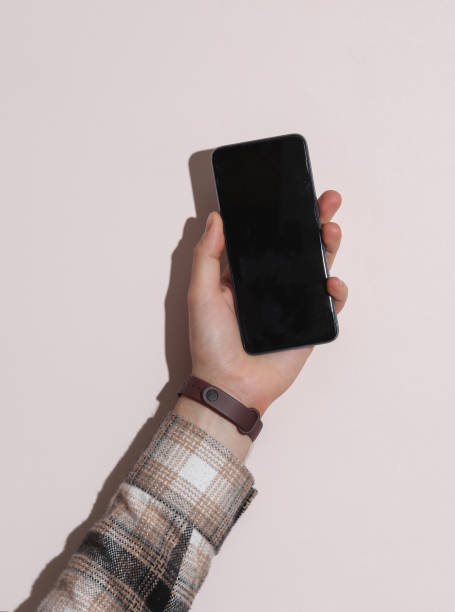 istock Man's hand in shirt holding smartphone on beige background with shadow 1780380504