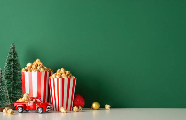 istock Spice up your winter holidays with popcorn delivery theme. Side view presents table featuring festive car, striped popcorn buckets, baubles, petite fir, green wall backdrop, allowing for movie promo 1780388234
