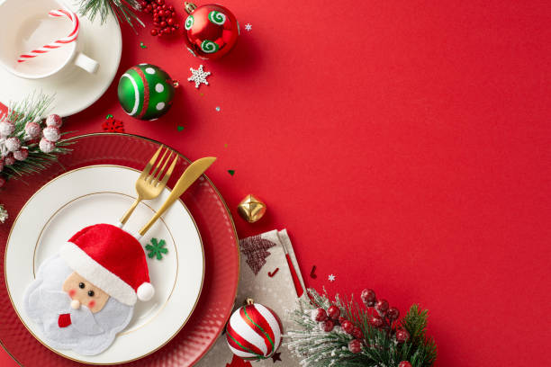 istock Craft delightful New Year's dinner table setup. Top view plates, charming gold cutlery in playful pocket, napkin, mug, candy cane, ornaments, frosted fir twigs, mistletoe on red backdrop with ad space 1780388771