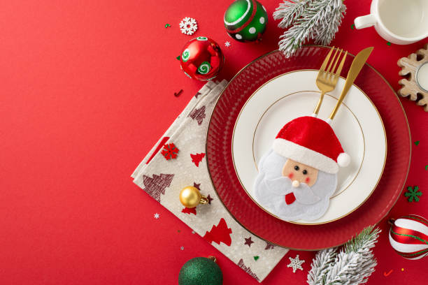 istock Create pleasurable New Year's dinner table setup. Top view of plates, whimsical gold flatware in quirky pocket, napkin, mug, ornaments, snowflake confetti, frosty fir sprigs on red backdrop for promo 1780388781