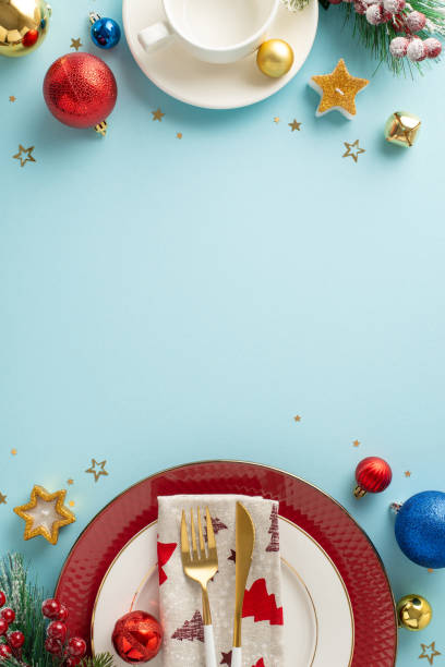istock Festive Christmas vertical top view table setting with plates, flatware, napkin, cozy mug, sparkling ornaments, candlelit star, confetti, frosted fir twigs on soft blue backdrop for your holiday joy 1780388830