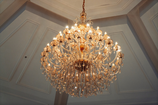 Beautiful chandelier hanging from ceiling. Classic gold plated design with glass crystals. Bright lights viewed from below with classy glass expensive bulbs.