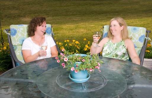 Two pretty women laughing over a glass of wine on the patio