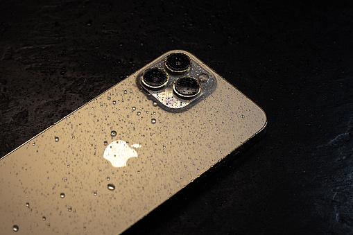 Kyiv, Ukraine - October 20, 2023 : Modern smartphone Apple iPhone 15 Pro with water drops on black background. Water resistant modern technology.