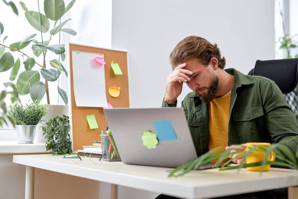 istock Tired guy sit working on laptop in modern office having deadlines, hard work alone 1780412128
