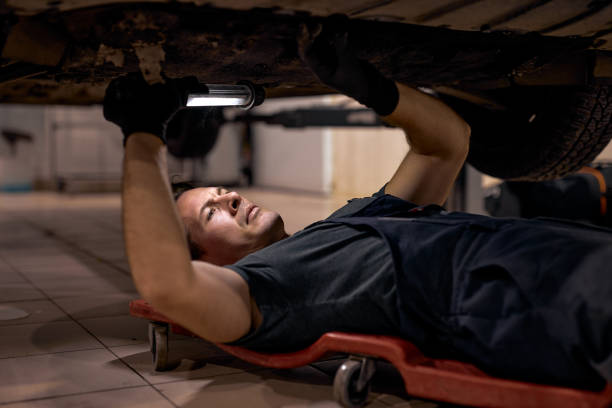 istock skilled mechanic in uniform is working in auto service with lamp, on floor 1780413256
