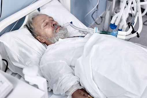 elderly caucasian european man suffering from coronavirus or covid-19. bedridden male patient on medical couch in modern hospital, alone, indoors. medicine, healthcare, treatment concept