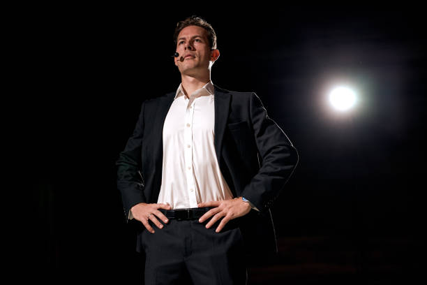 young attractive and confident successful guy speaking at corporate business coaching and training auditorium conference room talking giving motivation training from speaker stage. success concept
