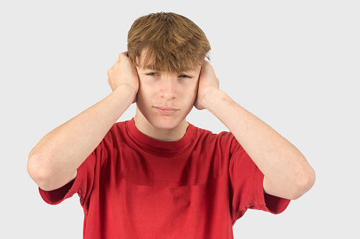 A studio portrait of a fifteen year old teenage boy covering his ears