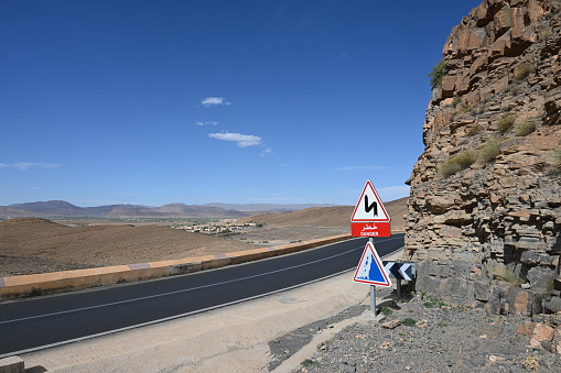 Warning signs on a winding road in the Atlas Mountains in Morocco. Beautiful but arid landscape under a blue sky.