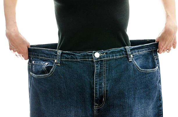 Woman showing how much weight she lost Woman showing how much weight she lost by wearing her old jeans. Weightloss concept. too thin stock pictures, royalty-free photos & images