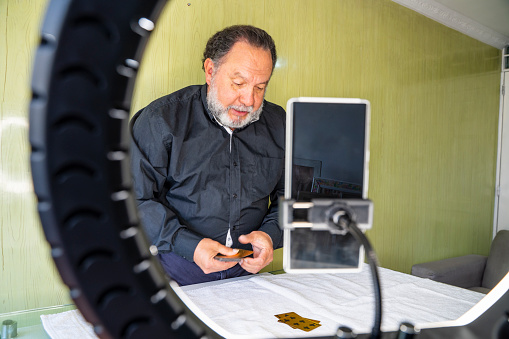 Old man of Latin ethnicity aged between 60-70 years is doing video blogging at home