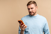 Scared frustrated man reding message in smartphone looking at screen on beige background.