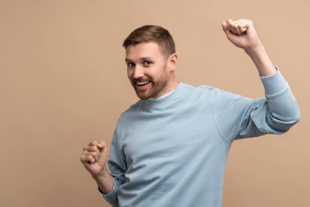 istock Overjoyed happy man showing win victory gesture on beige background looking at camera. 1780448381