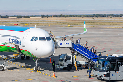 Bishkek, Kyrgyzstan - September 26, 2023: People walking on airstairs to the Uzbekistan Airways UK32105 plane Airbus A321-253NX plane at the Manas International Airport