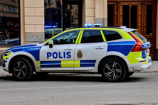 Stockholm, Sweden – April 04, 2023: A Swedish police car with blue lights on parked beside a public building