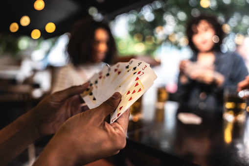 A man's hand holding a pair of playing cards with stack casino chips and revealed cards on a surface