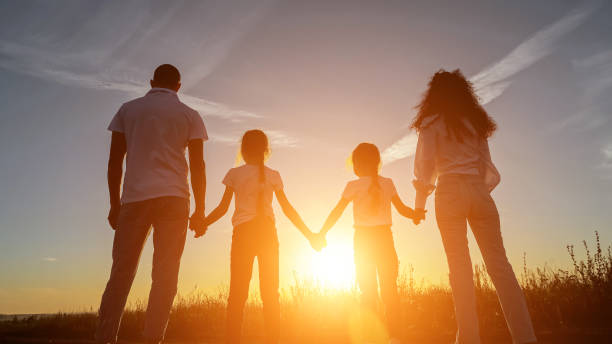 istock Sun rays fall on family holding hands in field at sunset 1780484647