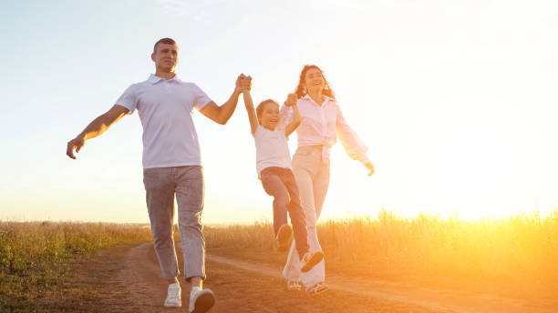 istock Parents lift daughter taking hands walking in field at sunset 1780484814