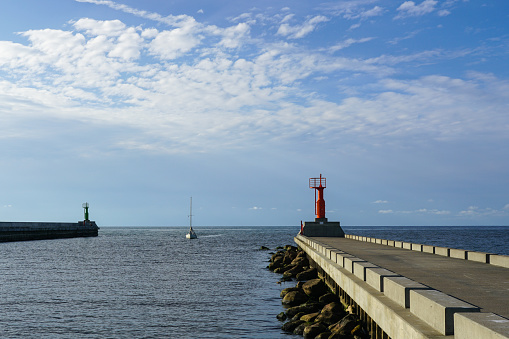 New, modernly equipped piers of a small port, a yacht sails into the port, blue sky background