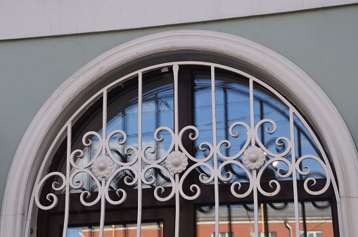 The window is arched, with a beautiful white openwork grille. Element of the facade of a city building.