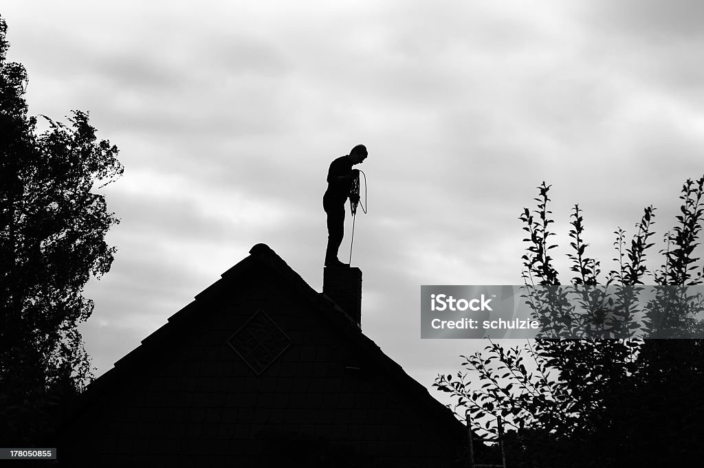 Chimney sweeper working on the roof Contour of a chimney sweep, silhouetted against the light.Black and white photo. Chimney Sweep Stock Photo