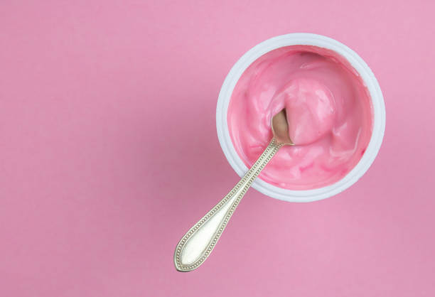 Strawberry pink yogurt in small plastic cup with little spoon isolated on pink background with copy space