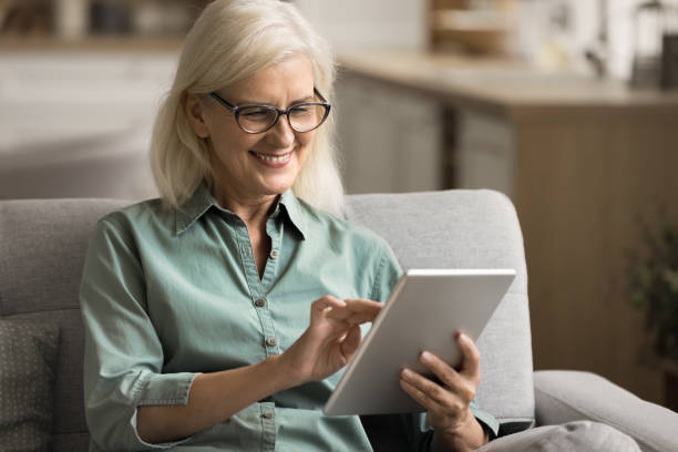 istock Positive elderly woman using digital gadget on home sofa 1780510356