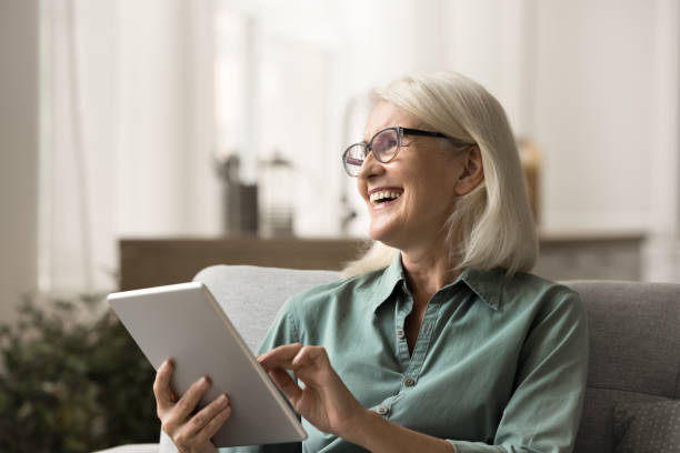 istock Cheerful elderly woman resting on home sofa with tablet 1780510365