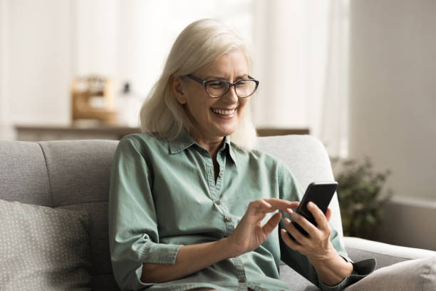 istock Cheerful blonde old retired woman in glasses using mobile phone 1780510367
