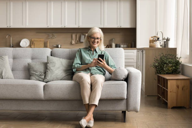istock Positive elderly lady relaxing on comfortable sofa with mobile phone 1780510376