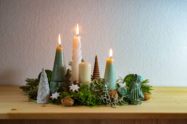 istock Third Advent, decoration with four different candles, three are lit, some moss, green Christmas balls from glass and cinnamon stars on a wooden board against a light wall, copy space 1780514542