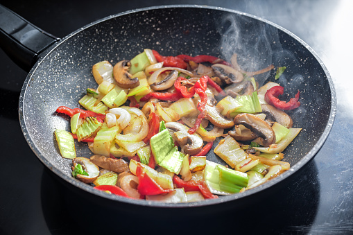 Steaming vegetables are stir-fried in a frying pan with healthy ingredients such as peppers, mushrooms, onions and cabbage, selected focus, narrow depth of field