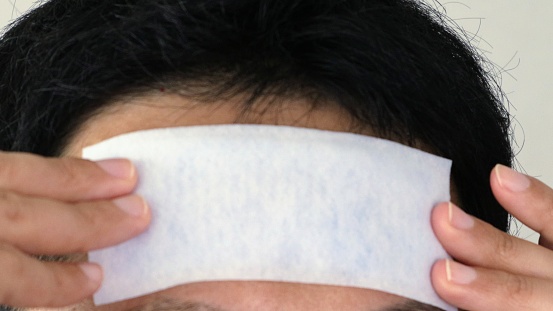 Close-up of a Japanese man applying a cooling sheet to his forehead