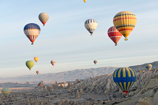 A red and green hot air balloon suspending a wicker basket slowly loses altitude to come in for a landing in the rocky desert near Marrakech in Morocco.