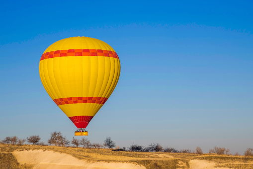 A red and green hot air balloon suspending a wicker basket slowly loses altitude to come in for a landing in the rocky desert near Marrakech in Morocco.