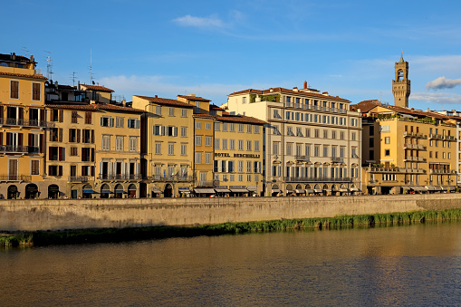 Florence, Italy - April 16, 2023: The historic architecture of the city can be seen here on the banks of the Arno river. The buildings here are illuminated by the rays of the slowly setting sun.