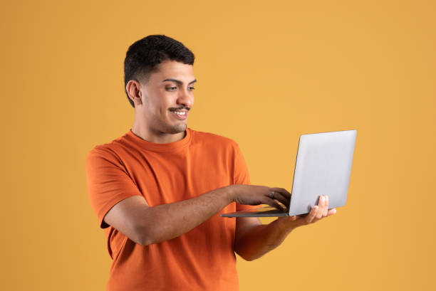 istock Happy brazilian man using laptop computer and browsing internet, trading posing standing over yellow background 1780537114