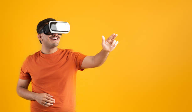 istock Excited man in VR glasses gesturing and interacting with cyberspace on yellow background, panorama, free space 1780537166