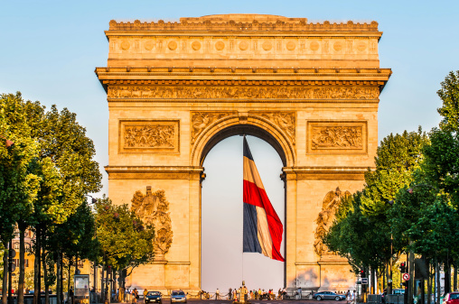arc of triumph with the french flag floating in the city of Paris in france