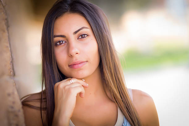 young woman sitting on a bench in the park with a distant look on her face, wearing a white sweater and a light yellow shirt, with long, curly hair