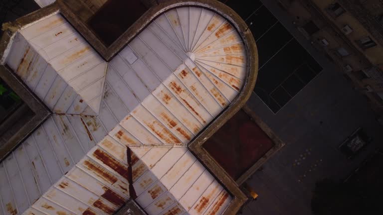 The drone flies low to the rusty cross-shaped roof of the church, diagonal composition