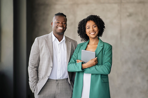 Business Partnership. Cheerful African American Coworkers Pair Posing With Digital Tablet Standing And Smiling Looking At Camera In Office, Wearing Formal Outfits. Successful Career, Employment