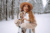 Fashionable woman in a stylish coat and hat holds sparklers in her hands in a snowy forest.