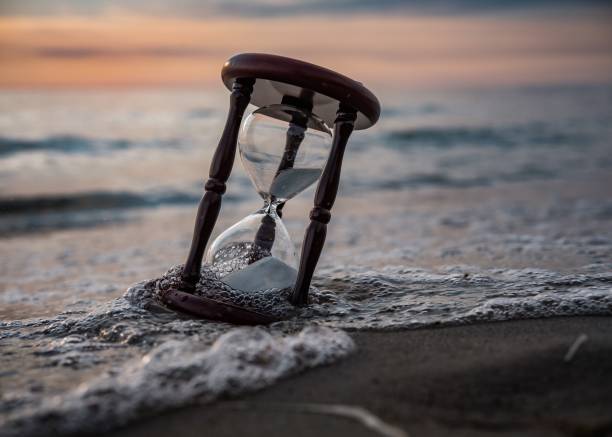 istock a hourglass standing on the sand by the beach at sunset 1780616721