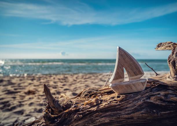 деревянная игрушка-корабль на бревне на пляже с голубым небом - logboat стоковые фото и изображения