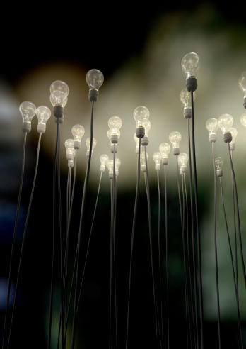 A group of regular light bulbs attached to cables reaching skyward creating an eerie greenish foggy glow on a dark background