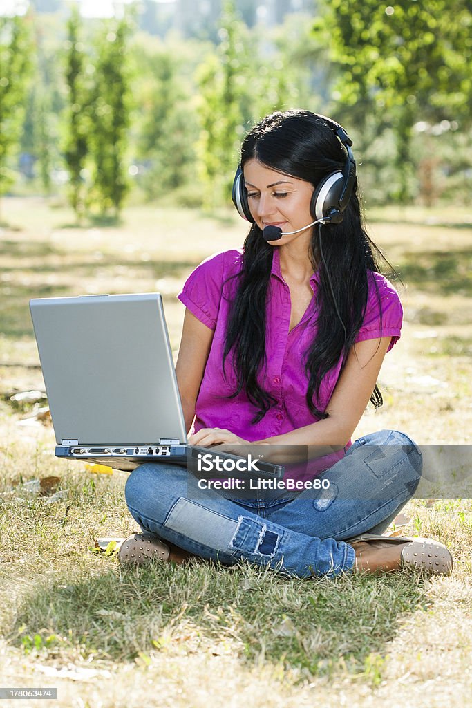 Woman with headset using laptop Beautiful woman with headphones sitting in the park and using laptop. Accessibility Stock Photo