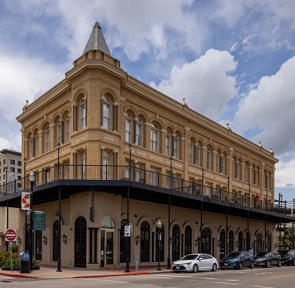 Galveston, United States – May 14, 2022: A modern high-rise building stands in the center of a bustling city street surrounded by parked cars in the historic Galveston area.