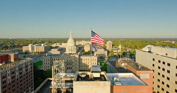 Aerial shot of downtown buildings in Lansing, Michigan on a sunny Fall morning, including the state capitol building with American and Michigan state flags flying.